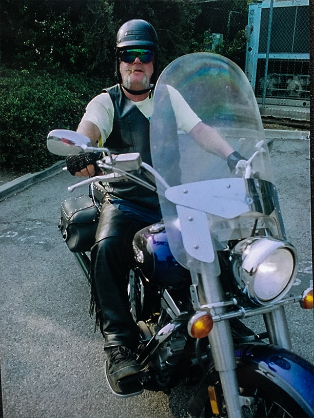 Spatz on his motorcycle wearing the prototype avatar skullcap, black leather vest and chaps, fingerless mesh gloves, rainbow-tint wraparound mirror glasses and smoking a black and mild.